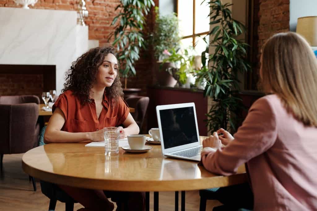 Women with Cups of Coffee and Laptop Sitting at Table providing references during an interview. 
