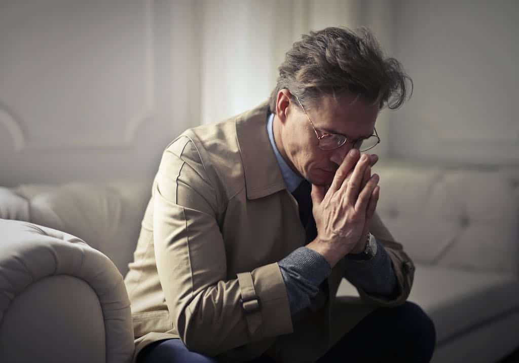 male in formal wear sitting on couch in contemplating the overuse of people-pleasing phrases at work